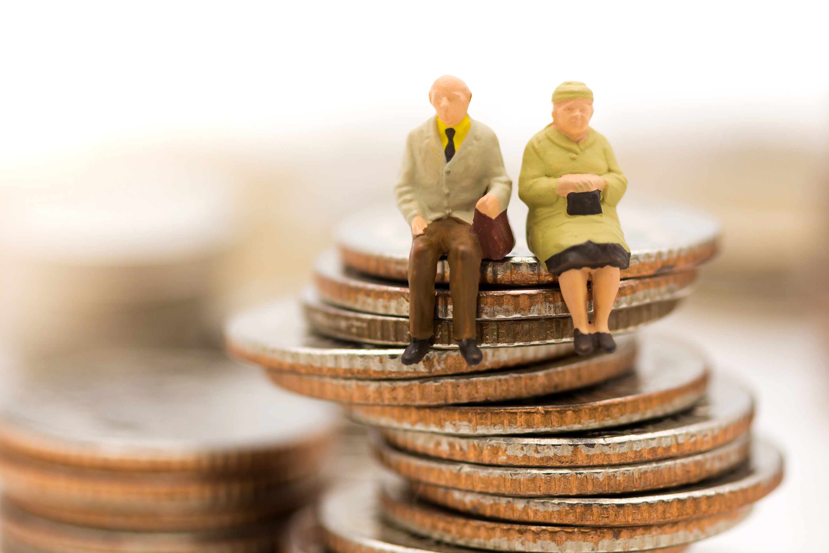 Image of an elderly couple of dolls sitting on a stack of coins. 