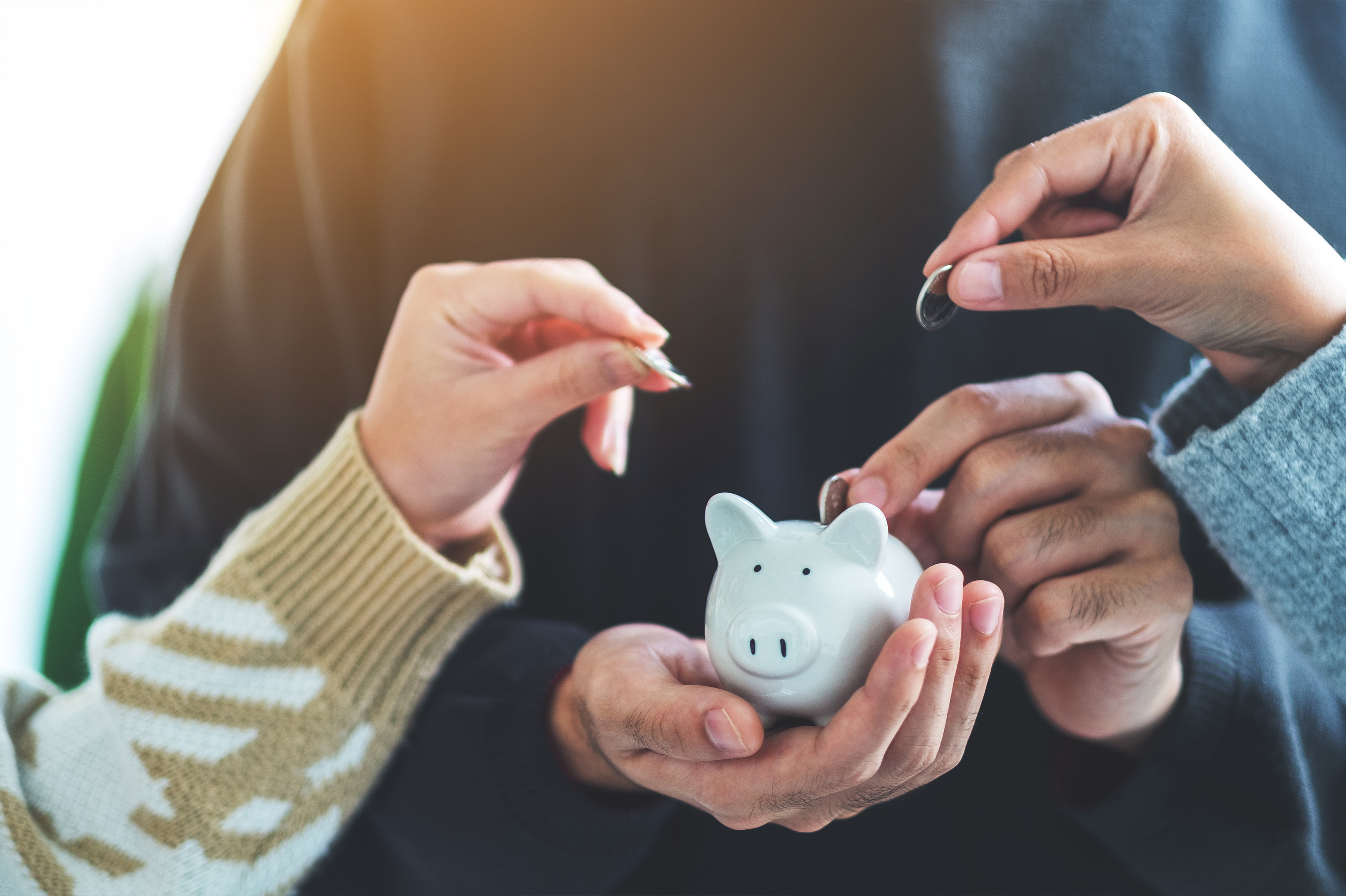 Image of people putting coins in a piggy bank. 