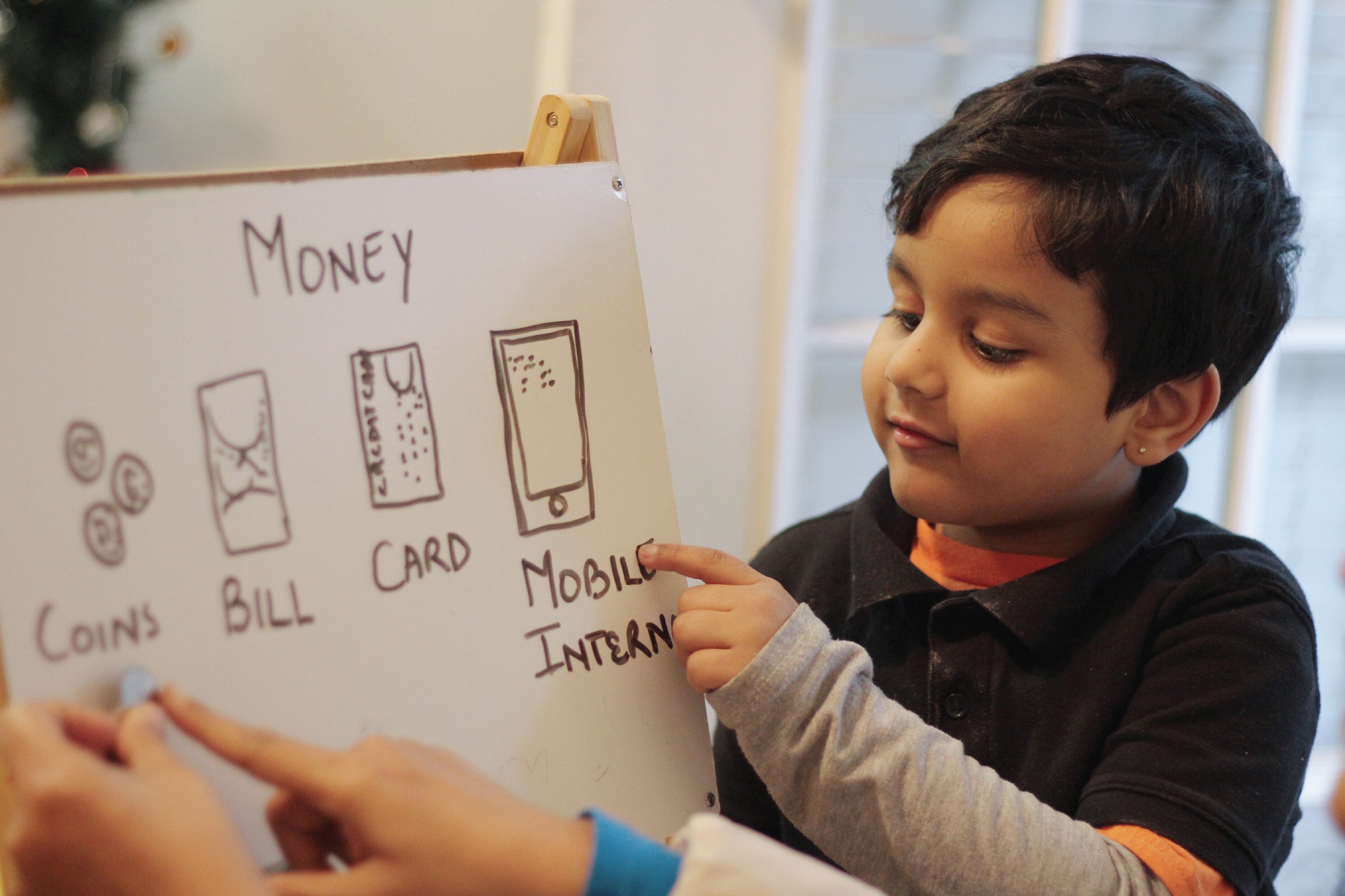 Child pointing to a board with types of currency on it