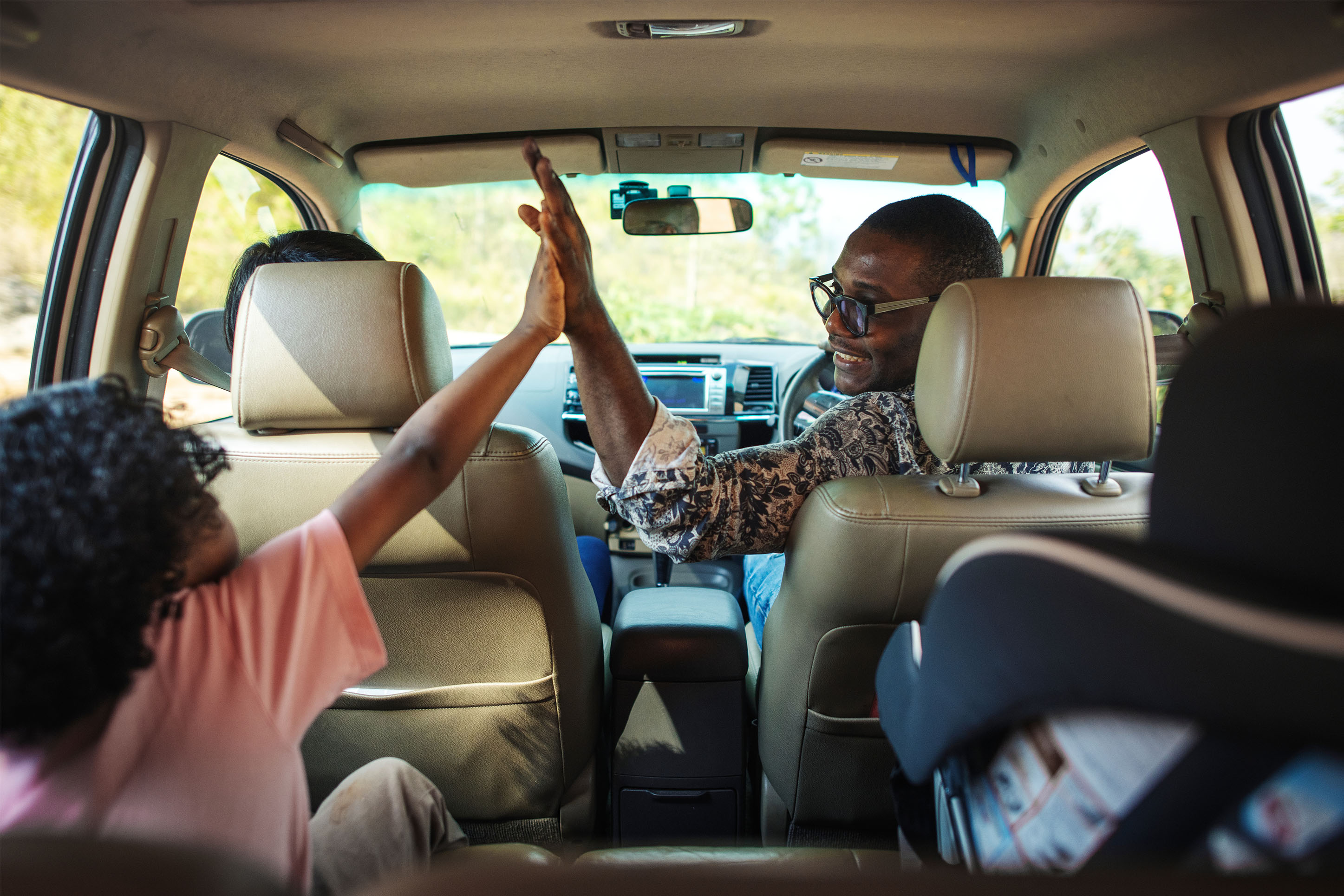 Family high-fiving in a car on a road trip. 