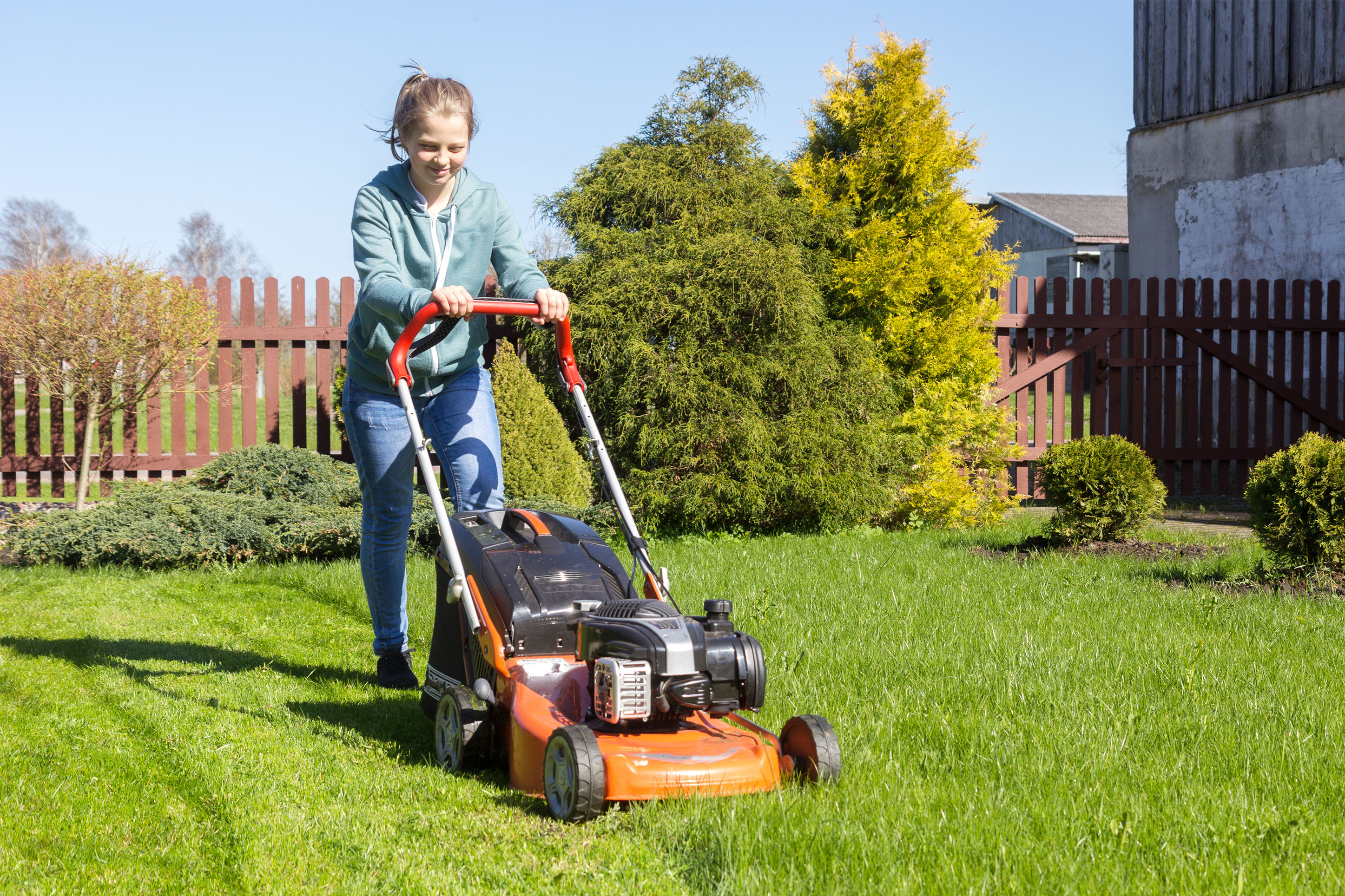 Young woman mowing a lawn for extra money. 